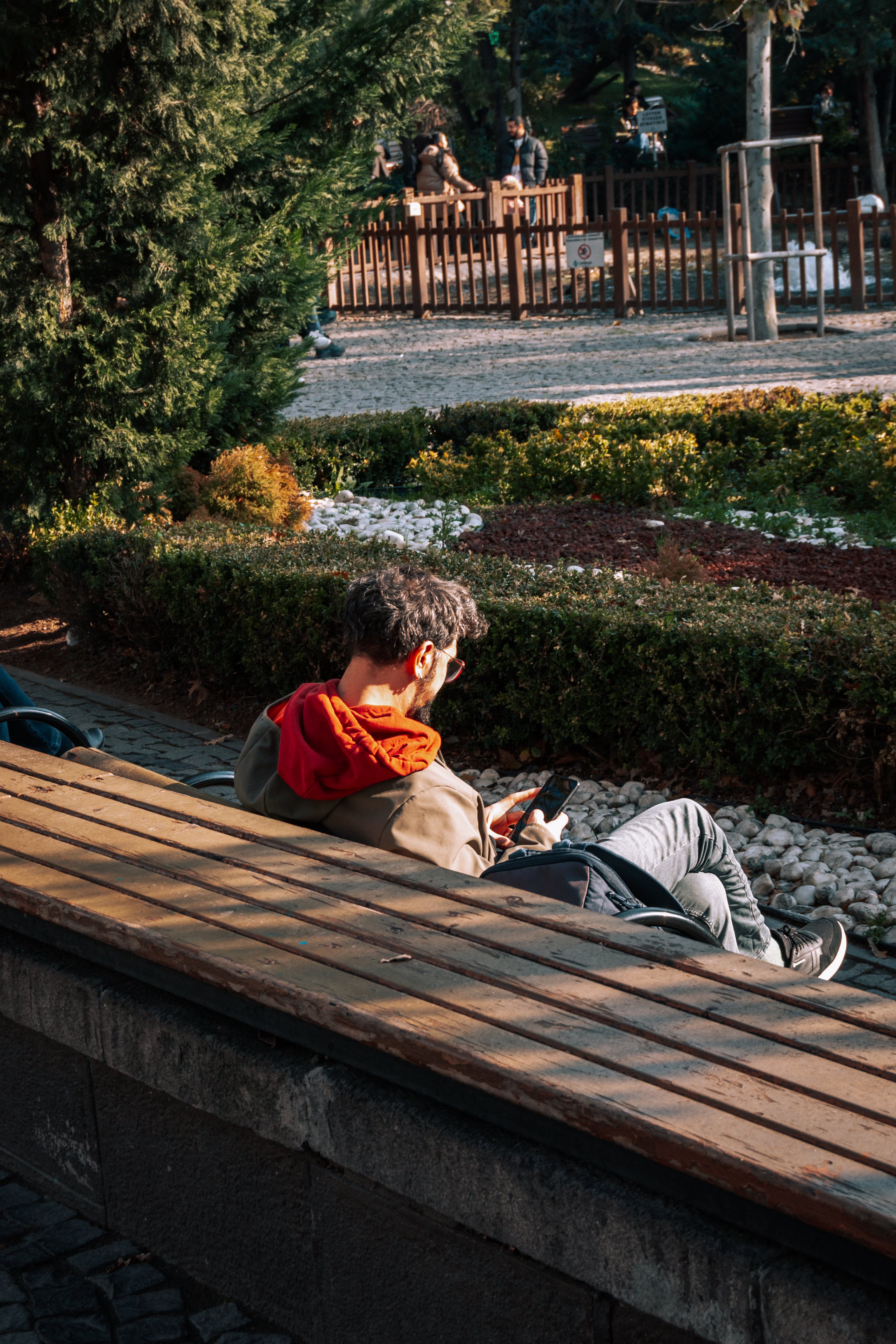 Foto van man op bankje die op smartphone kijkt, van een afstandje van achteren gefotografeerd.