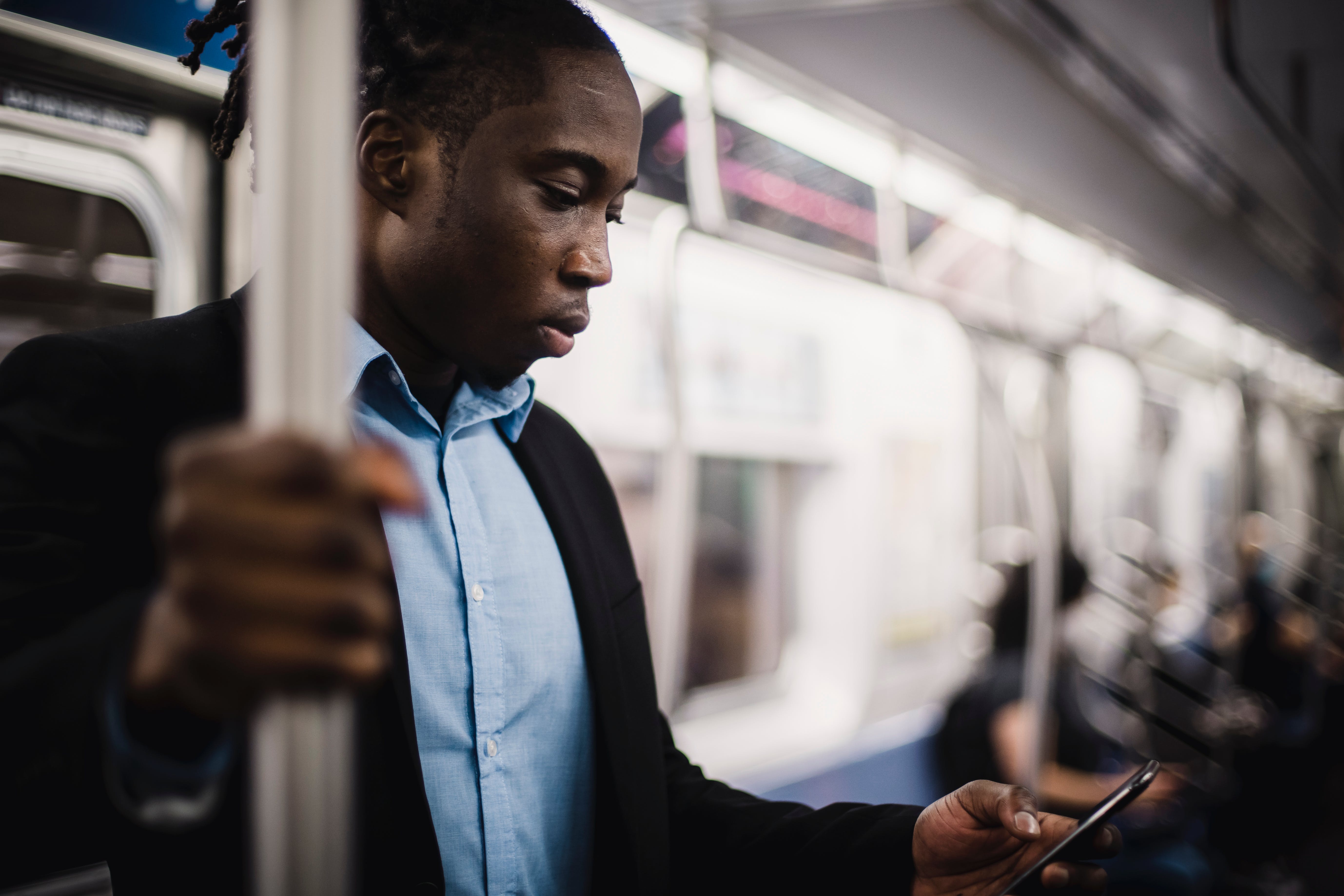 Foto van staande man in metro die op smartphone kijkt.