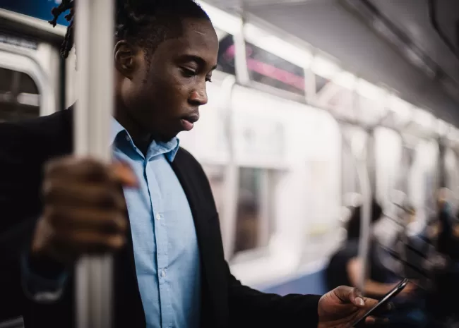 Foto van staande man in metro die op smartphone kijkt.